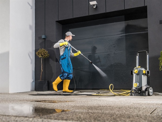 A person wearing overalls skillfully employing a pressure washer to safely clean different types of surfaces.