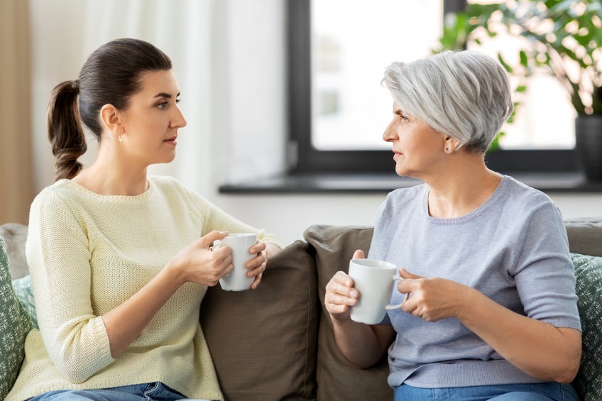 Adult daughter sitting on a couch having a civil, but serious, conversation with her elderly mother.